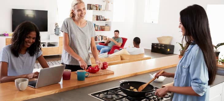 group of friends cooking, working and socialising in open plan kitchen