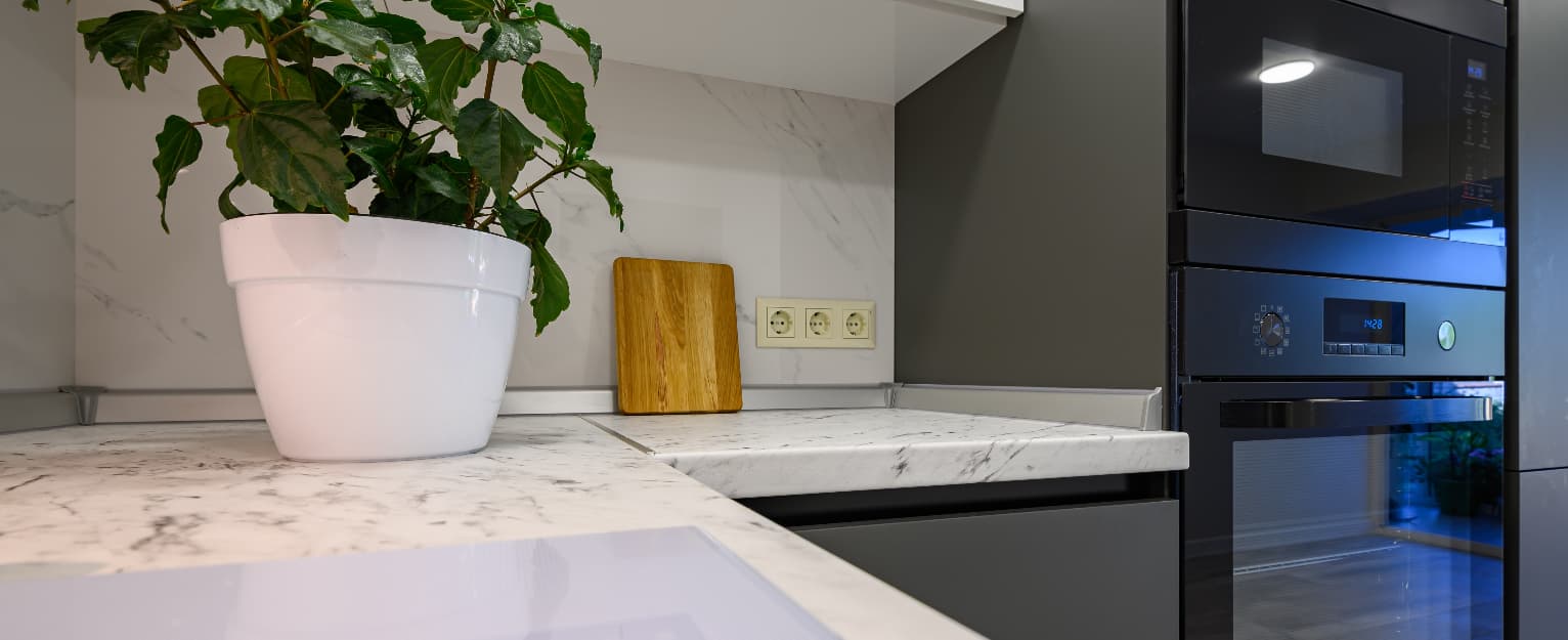 Modern kitchen with a marble worktop, built-in oven, and a potted plant on the counter.